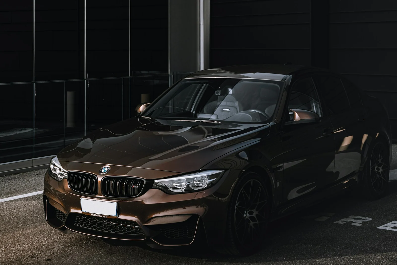 Czarne BMW M3 przy szklanej fasadzie budynku, fotografia Francesca La Corte